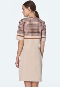 Beżowa sukienka z koronkowym gorsetem w kratę w odcieniach brązu i kremu, krótkimi rękawami z kontrastowymi paskami i prostą sylwetką w kształcie litery A.