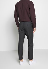 Camicia bordeaux a quadri con polsini con bottoni, indossata con pantaloni sartoriali grigio scuro e sneakers bianche, che mette in risalto una vestibilità contemporanea.