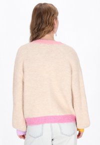 Pulover bej cu tiv și mansete în gradient de roz; textură moale și pufoasă; design supradimensionat cu umeri căzuți și mâneci lungi.