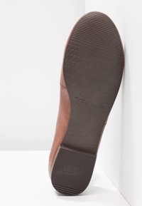 Semelle d'une chaussure en cuir marron avec semelle extérieure en caoutchouc à motifs montrant la marque Tamaris et un design antidérapant.