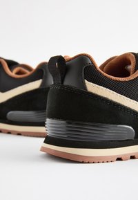 Baskets noires et marron avec une tige en daim et mesh, des accents texturés, une semelle en caoutchouc et un amorti au talon.