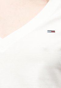 Λευκό T-shirt με V-λαιμόκοψη και μικρό ορθογώνιο λογότυπο με ναυτικό μπλε, λευκές και κόκκινες ρίγες στο στήθος.