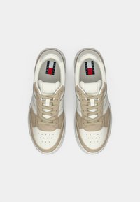 Pair of beige and white Tommy Jeans sneakers with laces, viewed from above on a plain white background.