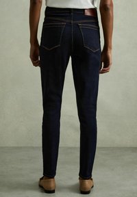 Mörkblå tajta jeans, denimtyg, femfickorsdesign, kontrasterande orange sömmar, läderetikett i midjan, figurnära silhuett.
