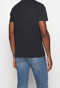 Černé bavlněné tričko s krátkým rukávem a jednoduchým kulatým výstřihem, nošené s světle modrými džíny. Viditelné švy a uvolněný střih.