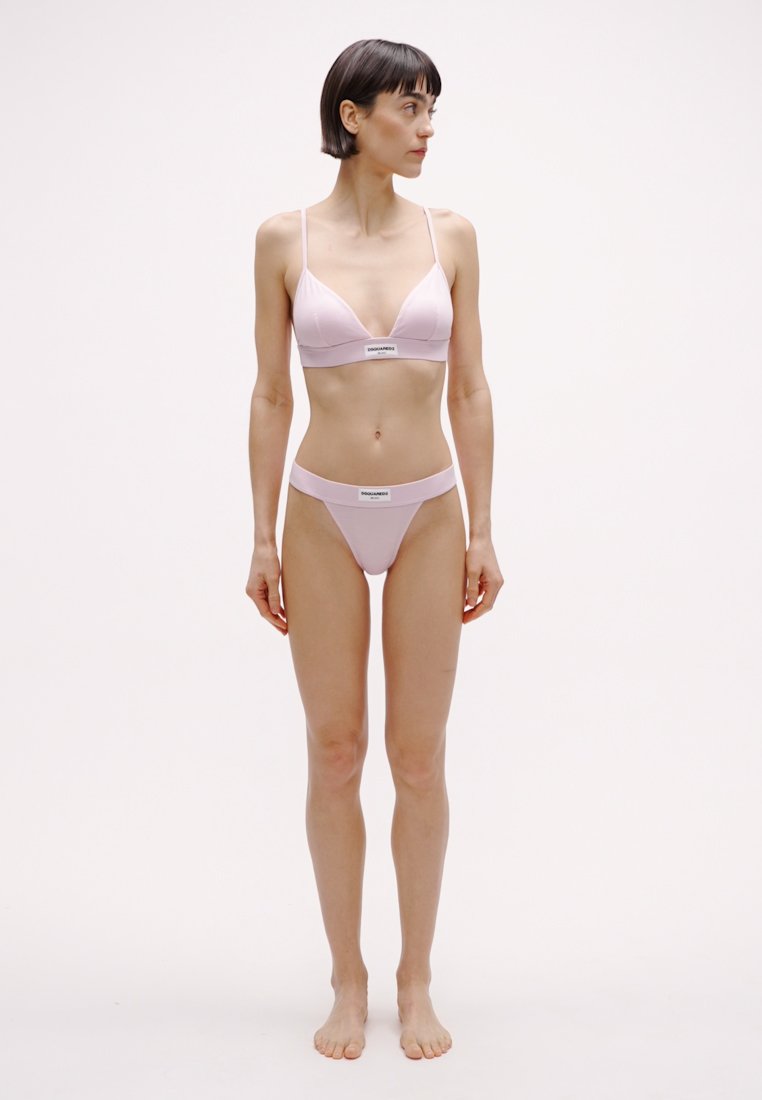Ensemble de lingerie rose pâle comprenant un soutien-gorge triangulaire et un string assorti. Texture lisse avec un design minimaliste et une bande élastique marquée.