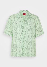 Chemise vert clair à manches courtes avec motif vertical en traits noirs et blancs et une étiquette rouge au col.