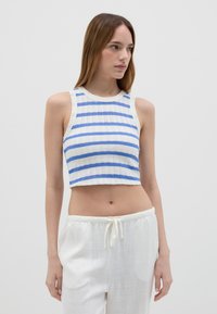 Top corto blanco con rayas azules, con tejido texturizado, cuello redondo y diseño sin mangas. Combinado con pantalones blancos con cordón.