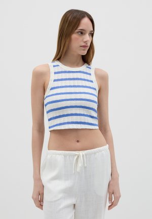 Top corto bianco con righe azzurre, realizzato in un tessuto testurizzato, con collo rotondo e senza maniche. Abbinato a pantaloni bianchi con coulisse.