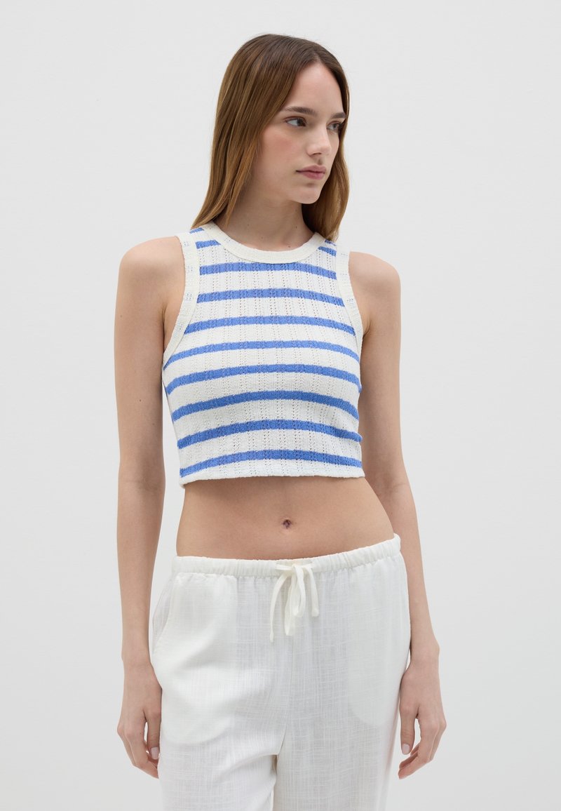Top corto blanco con rayas azules, con tejido texturizado, cuello redondo y diseño sin mangas. Combinado con pantalones blancos con cordón.