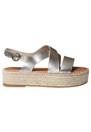 Metallic silver espadrille sandals with crisscross straps, adjustable ankle buckle, and woven jute platform sole. Smooth leather texture.