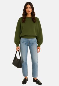 Olijfgroene sweatshirt met dropped shoulders, gecombineerd met lichtblauwe straight-leg jeans. Een zwarte handtas en loafers maken de look compleet.