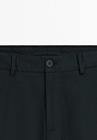 Černé kalhoty s plochým předním dílem, mají zapínání na knoflík, poutka na opasek a nenápadné detaily kapes. Vyrobené z hladkého materiálu.