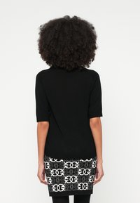 Μαύρο φόρεμα με κοντά μανίκια και υφασμάτινο διακοσμητικό σχέδιο στο τελείωμα σε λευκό χρώμα, με γραφικό σχέδιο. Λείο ύφασμα, εφαρμοστή σιλουέτα, μήκος μέχρι το γόνατο.