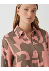 Camicia con colletto caratterizzata da un audace motivo geometrico in rosa e marrone. Realizzata in morbido tessuto con chiusura a bottoni e vestibilità comoda.