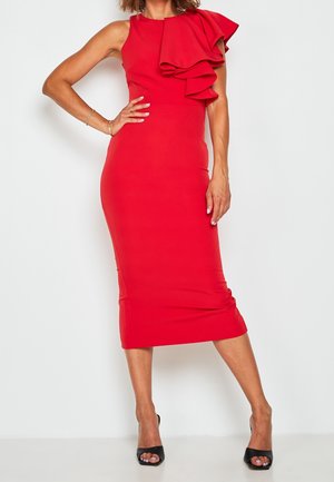 Nainen yllään hihaton punainen midimekko, jossa suuri röyhelöyksityiskohta yhdellä olkapäällä, yhdistettynä mustiin avoimilla varpailla varustettuihin korkokenkiin.