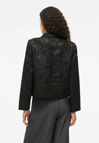 Veste noire cropped avec un motif floral texturé, fermeture à un bouton et manches droites. L'arrière est lisse avec un design minimaliste.