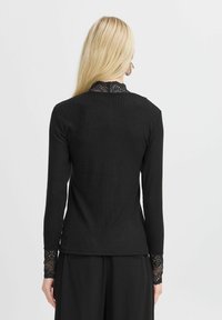 Schwarzes Langarmoberteil mit geripptem Material und Spitzenakzenten am Kragen und an den Bündchen, taillierte Passform und eleganter Schnitt.