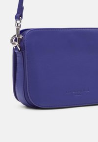 Borsa a tracolla viola in pelle con una texture liscia, dotata di accessori in argento, chiusura con zip e logo del marchio embossato sul davanti.