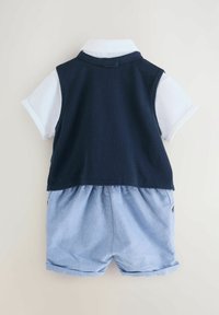 Jūras spēku bez piedurknēm vestē virs balta apkaklītes krekla, savienota ar gaiši ziliem denim šortiem. Iezīmē teksturētu vestu un rullētu piedurkņu apdari.