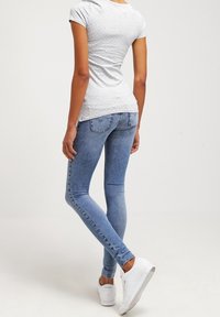 Top corto de manga corta gris claro con lunares blancos, combinado con jeans ajustados de mezclilla azul y zapatillas blancas. Tejido suave y diseño aerodinámico.