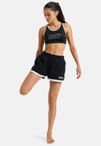 Sujetador deportivo negro con ribete blanco y logo "ROXY"; combinado con shorts negros con acentos blancos y una cinturilla elástica.