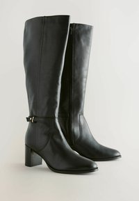 Botas de cuero negras hasta la rodilla con punta afilada, tacón cuadrado, zipper lateral y una correa ajustable cerca del tobillo.