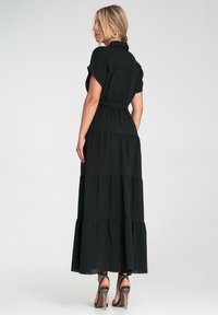 Czarna maxi sukienka z krótkimi rękawami, talią ściągniętą, warstwowym designem i przezroczystym materiałem. Połączona z sandałami na wysokim obcasie z paskami.