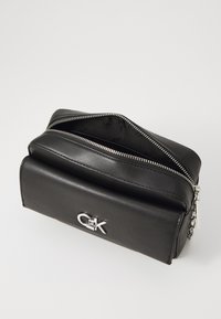 Borsa nera in pelle con zip argento e logo. Forma rettangolare, superficie liscia e una tasca esterna per lo stoccaggio.