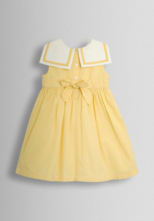 Kollase triibuga kleit valge kraega, millel on kollane ääris, nööpidega sulgur ja ees rippuv lips. Laiendatud seeliku disain.