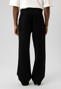 Zwarte denim broek met een hoge taille, wijde pijpen en achterzakken. De stof oogt stevig met een gladde textuur en minimale details.