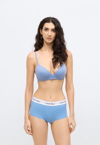 Ανοιχτό μπλε σουτιέν με λεπτές τιράντες και βαθύ ντεκολτέ, συνδυασμένο με ανοιχτό μπλε boyshort σλιπ με λευκή ζώνη μέσης και λογότυπο "Calvin Klein".