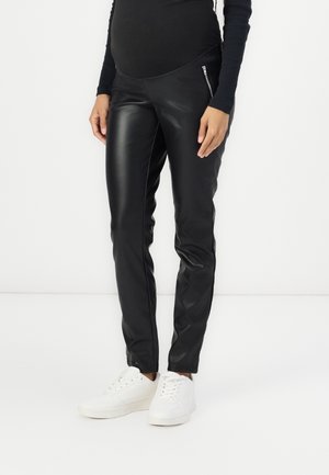 Black faux leather pants with a slim fit, featuring a high waistband, side zip pockets, and a smooth, glossy texture, paired with white sneakers.