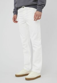 Jeans en denim blanc avec une coupe droite, des poches avant et une fermeture à bouton-zip. Associés à des baskets crème avec une semelle en caoutchouc.