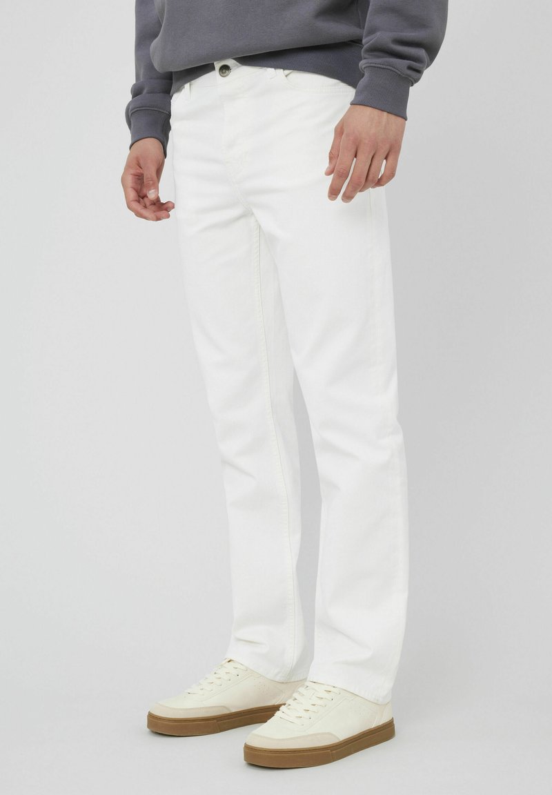 Jeans en denim blanc avec une coupe droite, des poches avant et une fermeture à bouton-zip. Associés à des baskets crème avec une semelle en caoutchouc.