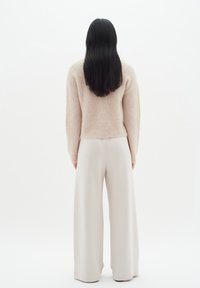Pull en beige et duveteux, large pantalon crème, texture lisse, ajusté à la taille, coupe ample, vue de dos sur un fond clair uni.