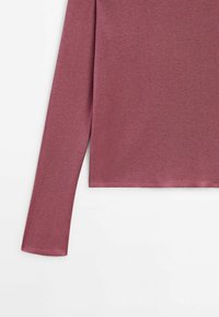 Haut à manches longues en rose poussiéreux, en tissu côtelé. Présente une silhouette ajustée avec un ourlet droit, une texture douce et sans accents visibles.