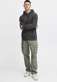Grauer Hoodie mit frontaler Kängurutasche und geripptem Saum, kombiniert mit olivgrünen Cargo-Hosen mit mehreren Seitentaschen und geradem Schnitt.
