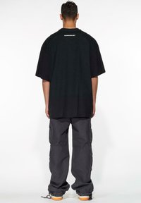 Svart oversized t-skjorte med en liten logo på baksiden, sammen med mørk grå cargosbukser med flere lommer og en smal nederkant.