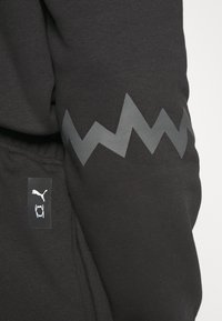 Musta huppari, jossa on tyylikäs harmaa sawtooth-kuvio hihassa ja pieni musta logotagi valkoisella symbolilla sivulla.