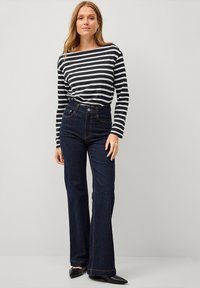 Zwart-witte gestreepte blouse met lange mouwen, gecombineerd met hoge donkere spijkerflared jeans. Zwarte puntige ballerina's. Eenvoudig ontwerp.