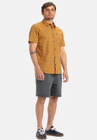 Short-sleeve shirt in orange with a hexagonal pattern, paired with gray shorts and navy sneakers. Button-down design with a collar.