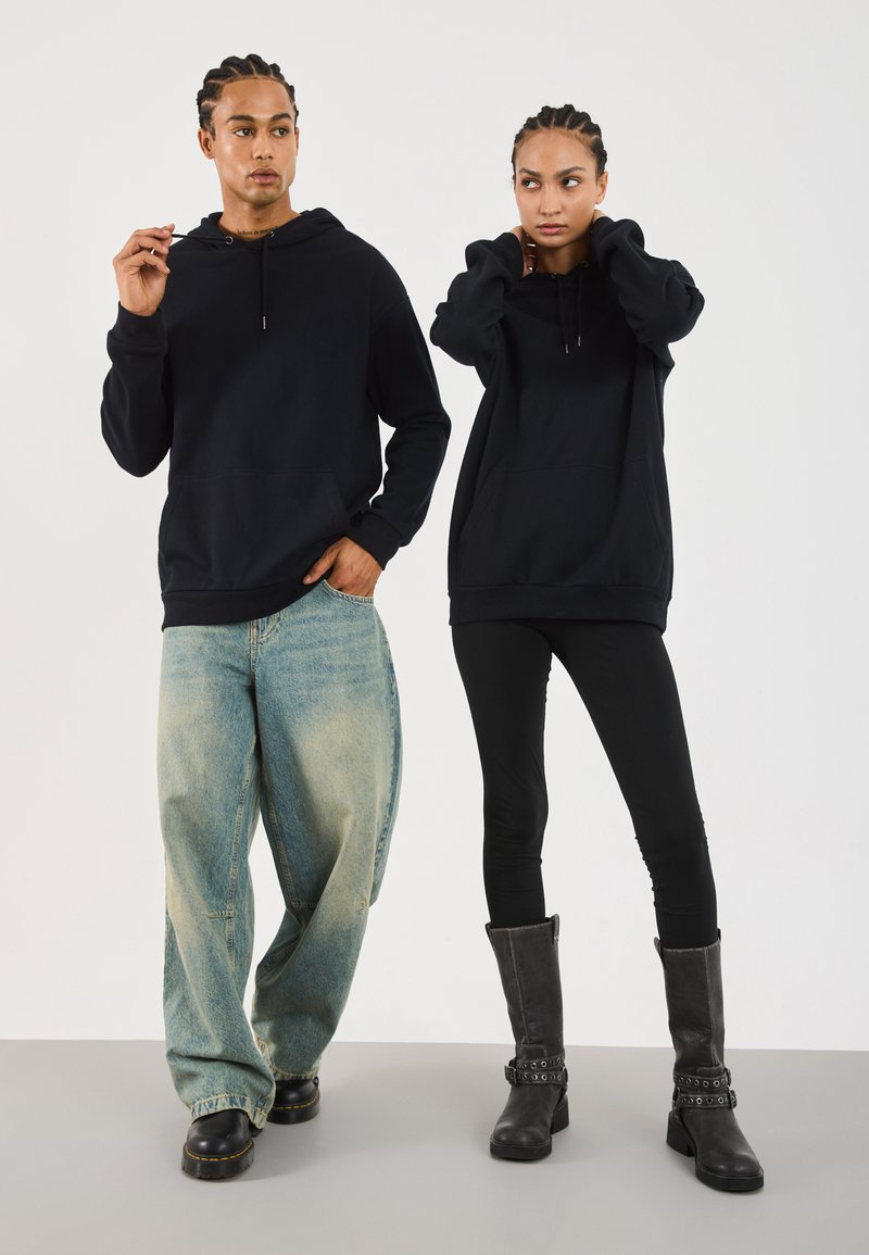Svarte hettegensere i avslappet passform. Lyseblå baggy jeans med slitte detaljer, svarte leggings og svarte støvler til knærne med spenneakkenter.