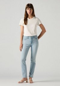 Jeans azul claro con corte ajustado y dobladillo recortado, combinados con una camiseta blanca de manga corta y sandalias crema de tiras. Textura lisa.