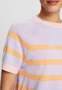 Person mit einem pastellgestreiften Kurzarmpullover in Lavendel, Pfirsich und hellem Rosa, der Details des Ausschnitts und des Oberkörpers zeigt.