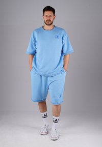 Light blue cotton athletic set featuring a short-sleeved top and knee-length shorts, both with stitched hems and a logo detail.