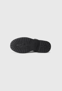 Talpă din cauciuc negru, cu un model texturat de profil, având caneluri și mici elemente decorative. Design plat, potrivit pentru diverse stiluri de încălțăminte.