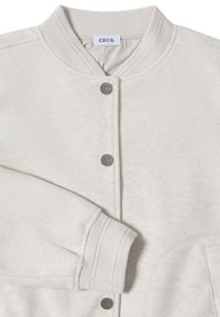 Helle Bomberjacke aus weichem, strukturiertem Stoff. Verfügt über einen gerippten Kragen und Bündchen, Druckknöpfe und Seitentaschen.