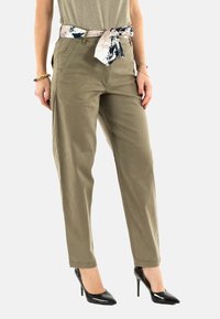 Pantalons vert olive à coupe décontractée et poches latérales, dotés d'une ceinture à motifs contrastants. Portés avec des chaussures à talons hauts noires.