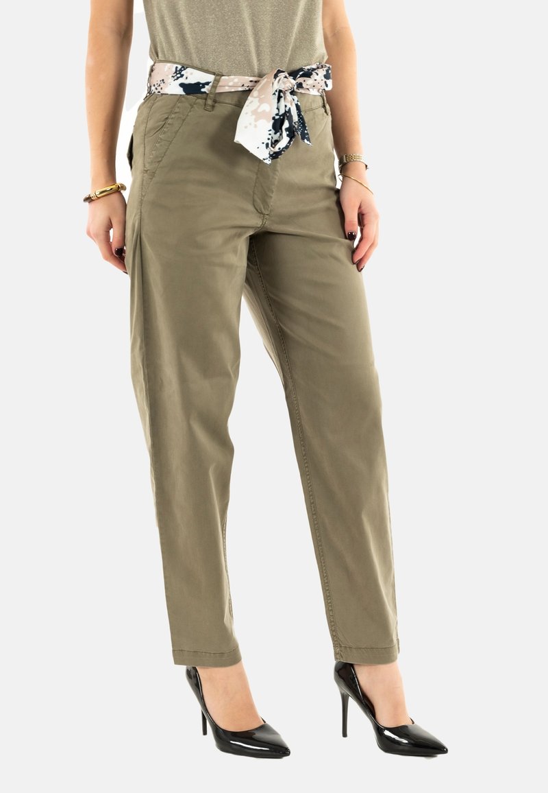 Pantalons vert olive à coupe décontractée et poches latérales, dotés d'une ceinture à motifs contrastants. Portés avec des chaussures à talons hauts noires.